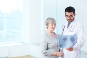 Senior patient looking attentively at x-ray held by radiologist in hospital